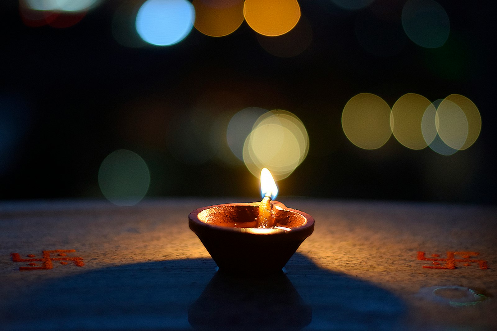 A lit clay diya with colourful lights in the background