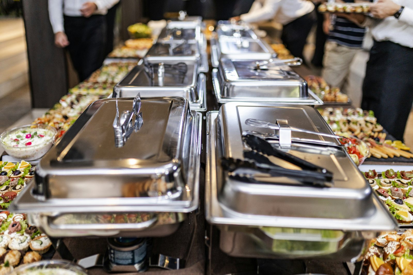 Stainless steel chafing dishes on a buffet table with assorted appetizers