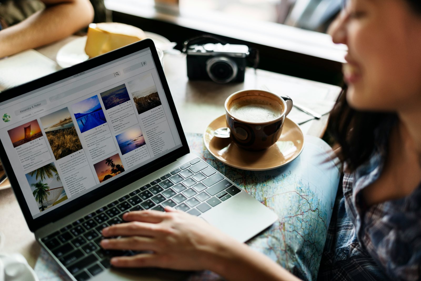 A person using a laptop on a map beside a coffee cup and a camera