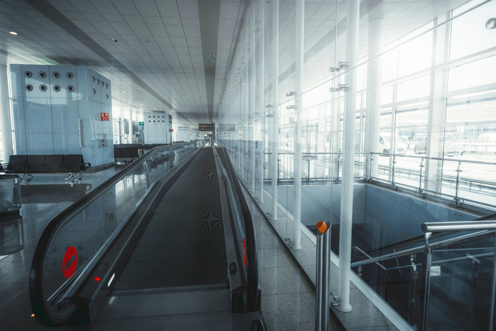 A moving walkway in a bright modern airport terminal with glass walls