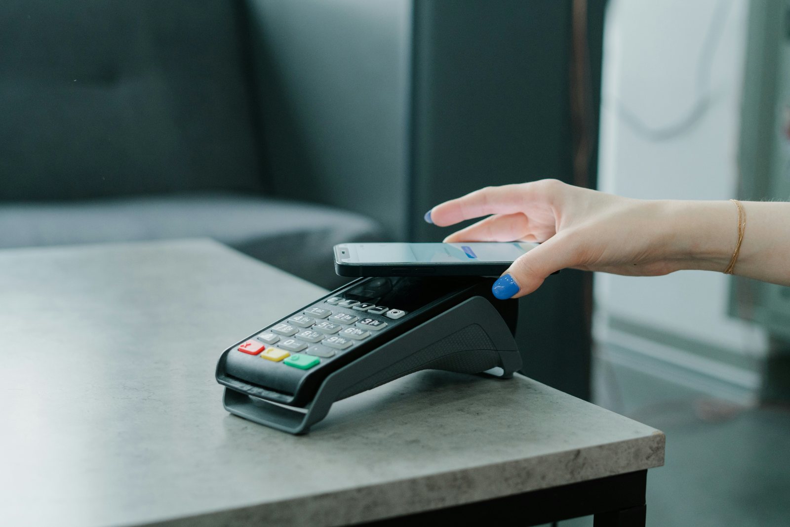 A hand holding a phone over a payment terminal at a counter